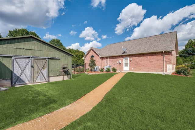 rear view of property featuring a barn, roof with shingles, a yard, an outdoor structure, and brick siding