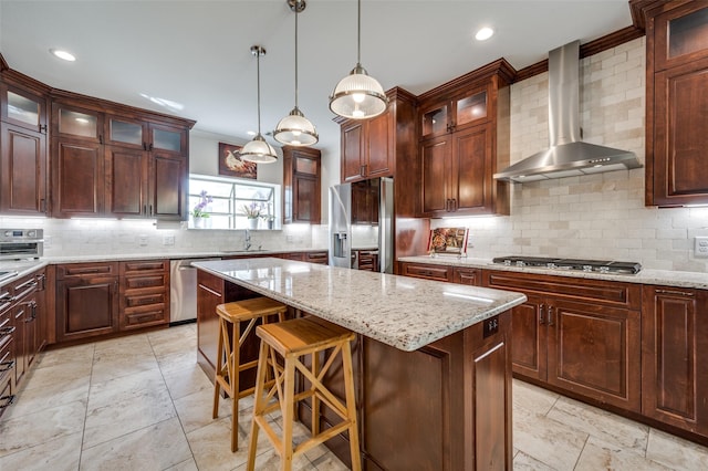 kitchen featuring tasteful backsplash, wall chimney exhaust hood, a kitchen island, stainless steel appliances, and a sink