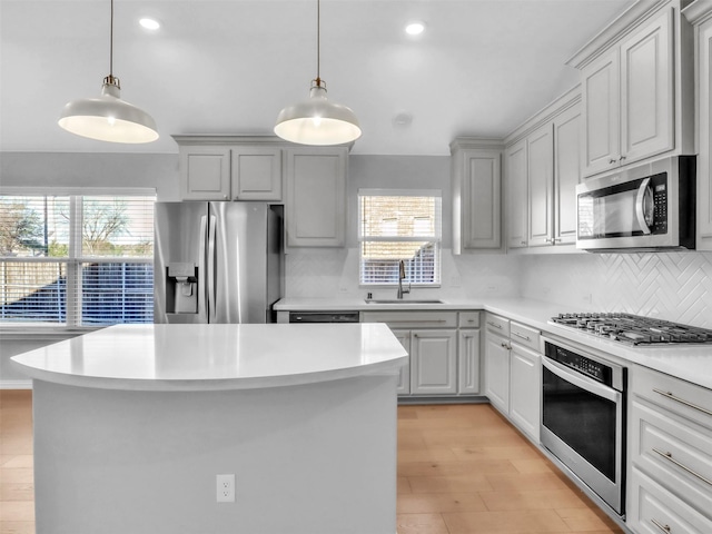 kitchen with stainless steel appliances, light countertops, decorative backsplash, a sink, and a kitchen island