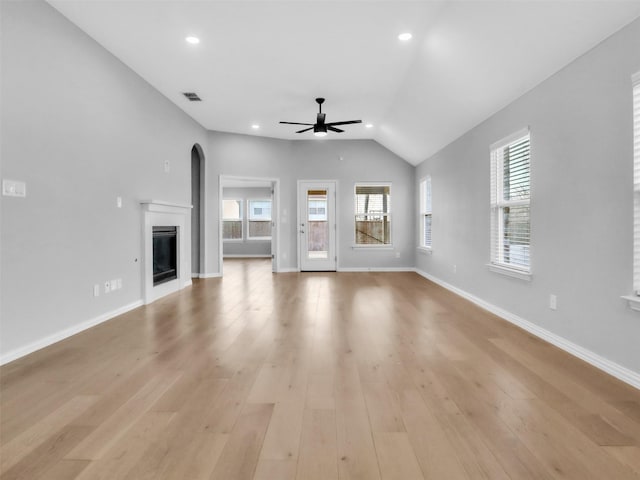 unfurnished living room with light wood-style flooring, visible vents, a wealth of natural light, and a glass covered fireplace