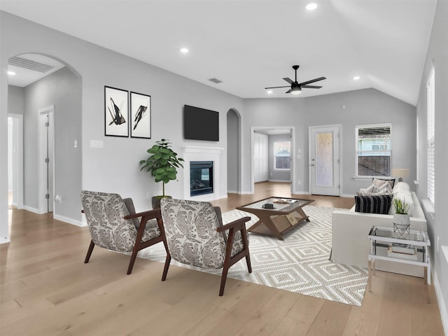 living area featuring arched walkways, a glass covered fireplace, lofted ceiling, light wood-type flooring, and recessed lighting