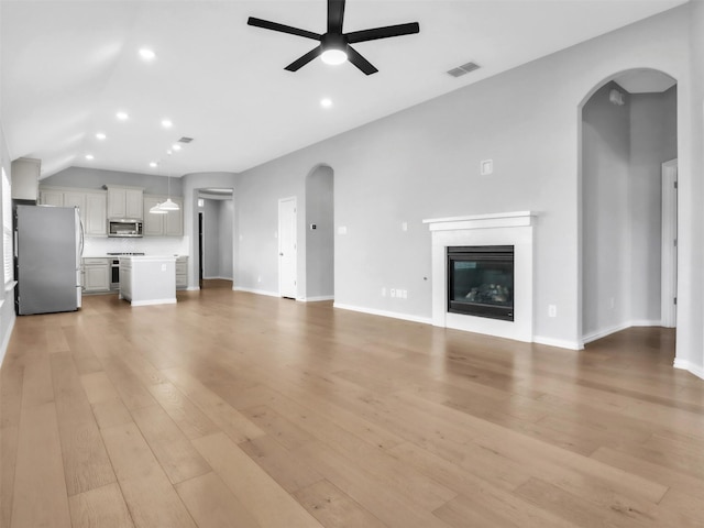 unfurnished living room with light wood finished floors, arched walkways, a ceiling fan, a glass covered fireplace, and recessed lighting