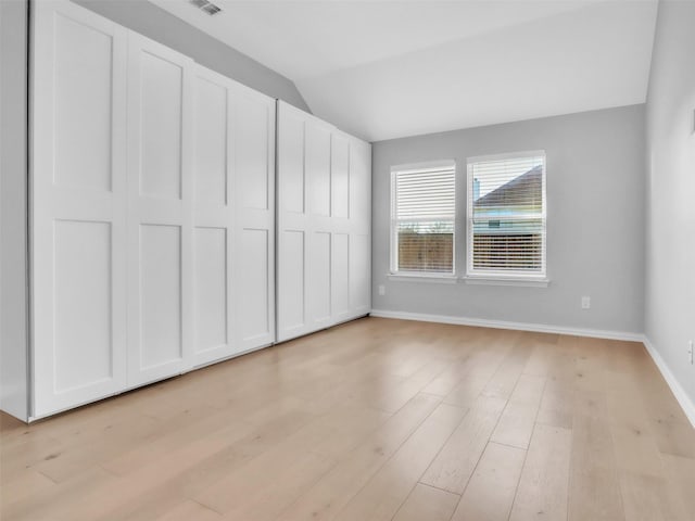 unfurnished bedroom with light wood-type flooring, vaulted ceiling, and baseboards