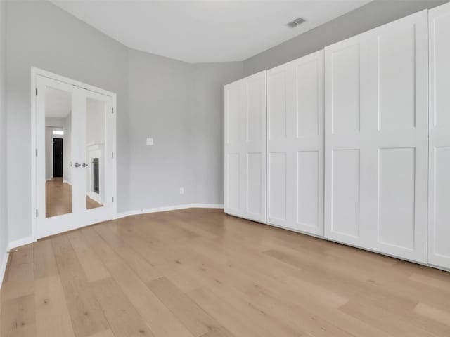 unfurnished bedroom featuring light wood finished floors, baseboards, visible vents, and a glass covered fireplace