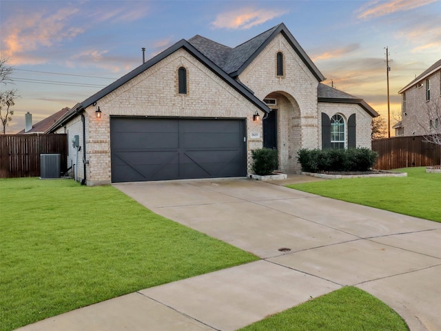 french country style house with concrete driveway, brick siding, and a lawn