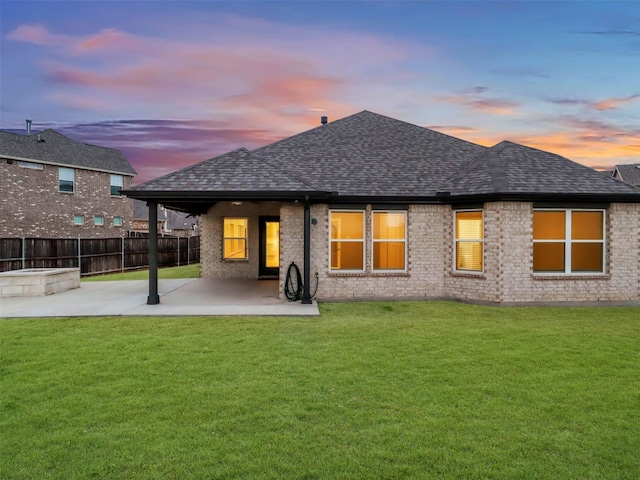 back of house at dusk featuring a patio area, a shingled roof, fence, and a yard