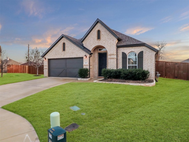 french country inspired facade featuring a garage, concrete driveway, brick siding, and a front yard