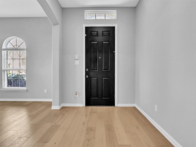 entrance foyer with light wood-type flooring, baseboards, and arched walkways