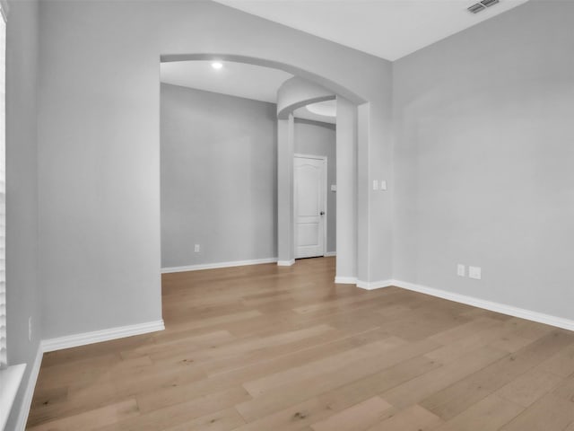 unfurnished room with light wood-style floors, arched walkways, and baseboards