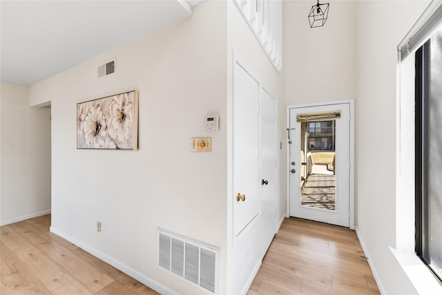 corridor with light wood finished floors, baseboards, and visible vents