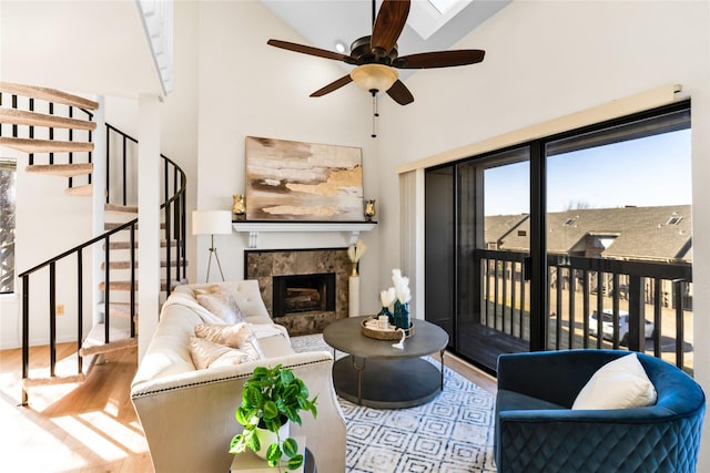 living area featuring ceiling fan, a fireplace, wood finished floors, a towering ceiling, and stairway