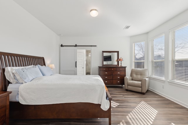 bedroom with a barn door, wood finished floors, visible vents, and baseboards