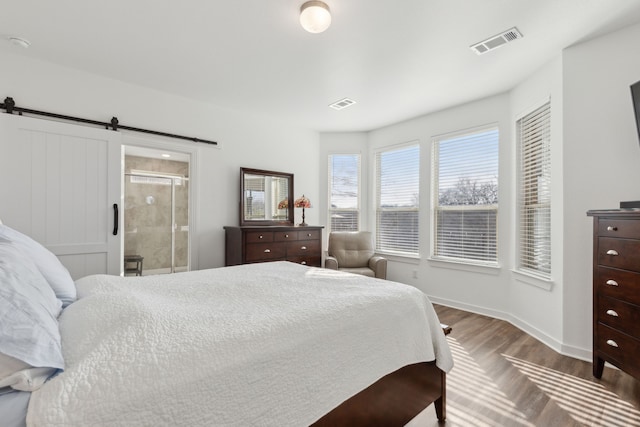 bedroom featuring a barn door, wood finished floors, visible vents, and baseboards