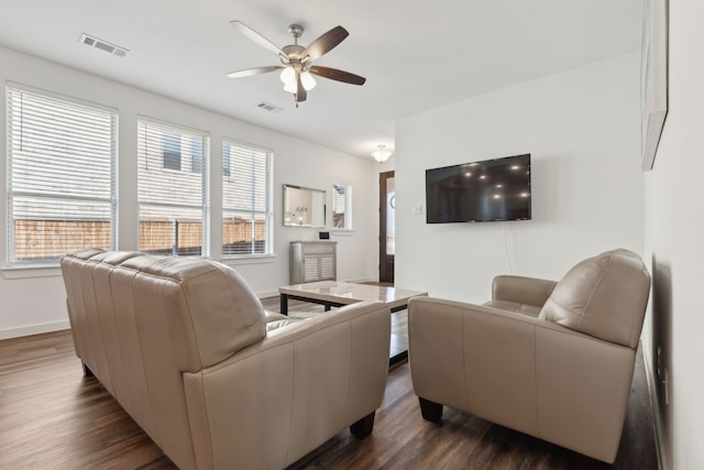 living room with dark wood-style floors, baseboards, visible vents, and a ceiling fan