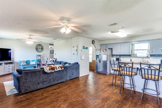 living area featuring ceiling fan, visible vents, dark wood finished floors, and a textured ceiling