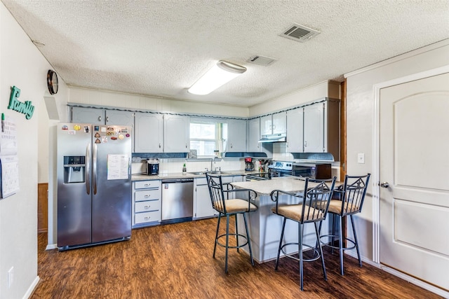 kitchen featuring under cabinet range hood, a peninsula, visible vents, appliances with stainless steel finishes, and dark wood finished floors