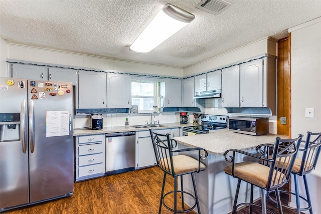 kitchen with stainless steel appliances, visible vents, a sink, a peninsula, and under cabinet range hood