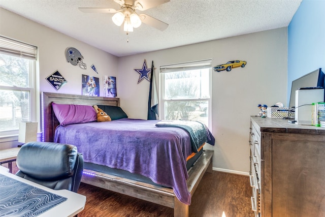 bedroom with a textured ceiling, multiple windows, baseboards, and wood finished floors