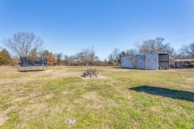 view of yard with an outdoor fire pit, a trampoline, and an outbuilding