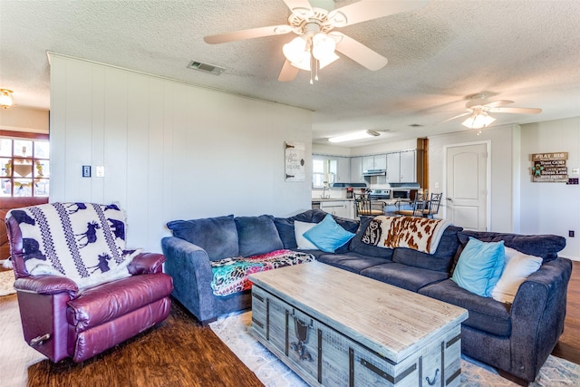 living room featuring visible vents, ceiling fan, a textured ceiling, and wood finished floors