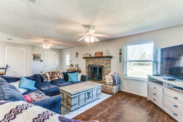 living room featuring a textured ceiling, a brick fireplace, wood finished floors, and a ceiling fan