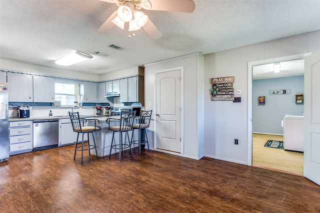 kitchen featuring under cabinet range hood, stainless steel appliances, a breakfast bar, visible vents, and dark wood finished floors