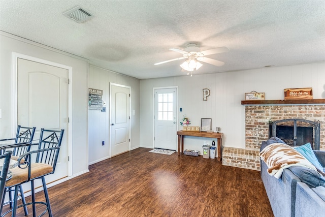 living area with a ceiling fan, a brick fireplace, visible vents, and wood finished floors