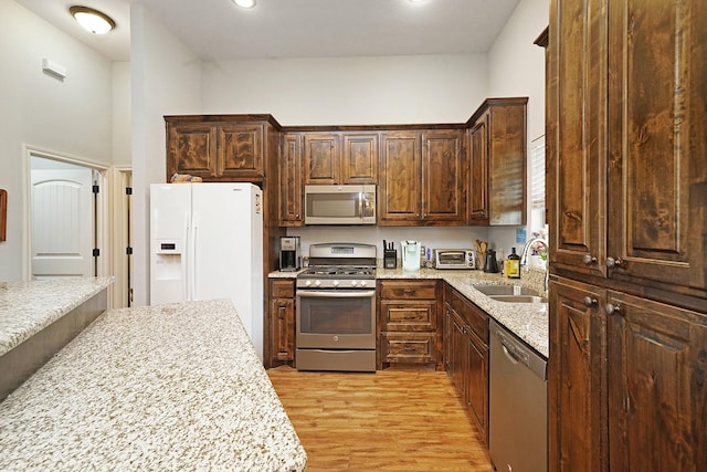 kitchen with light stone counters, stainless steel appliances, dark brown cabinetry, a sink, and light wood-type flooring