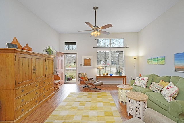 living area featuring ceiling fan, light wood-style flooring, and a towering ceiling