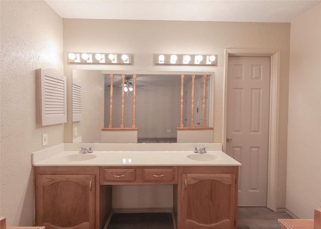 bathroom featuring ceiling fan, a textured wall, a sink, and double vanity