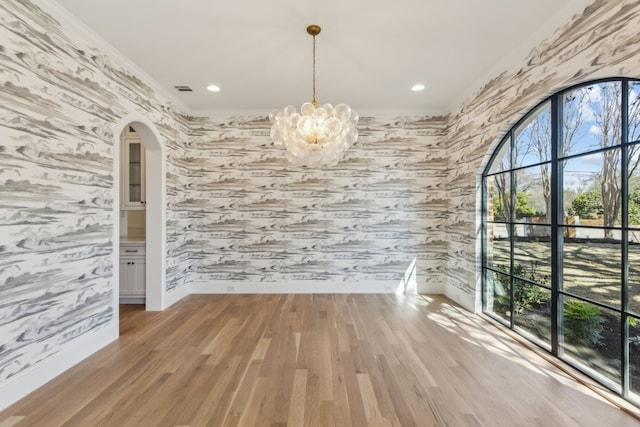 spare room with arched walkways, light wood-style floors, baseboards, wallpapered walls, and crown molding