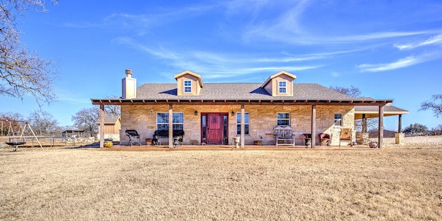 back of property with stone siding, a shingled roof, a trampoline, and a chimney