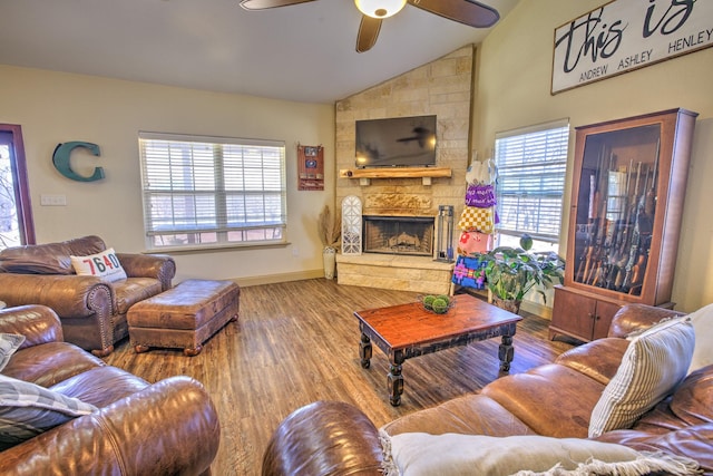 living area featuring baseboards, a ceiling fan, lofted ceiling, wood finished floors, and a stone fireplace