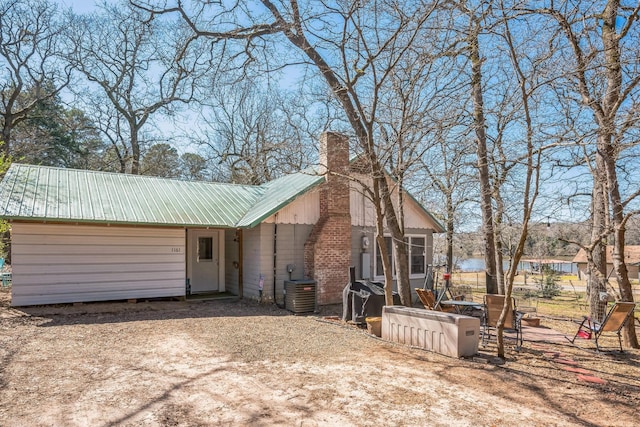 view of front of property with central AC unit, a chimney, and metal roof