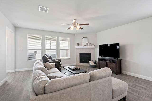 living room featuring ceiling fan, wood finished floors, visible vents, baseboards, and a tiled fireplace