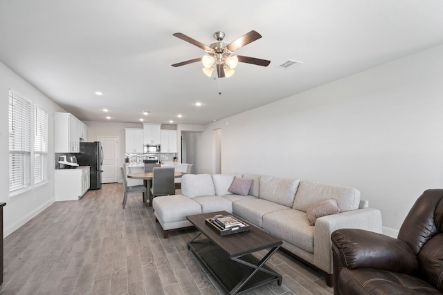 living room featuring visible vents, baseboards, light wood-style flooring, ceiling fan, and recessed lighting