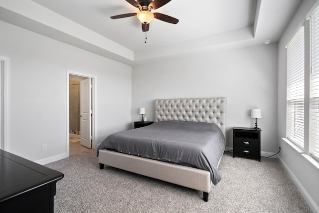 carpeted bedroom with baseboards, a raised ceiling, a ceiling fan, and ensuite bathroom