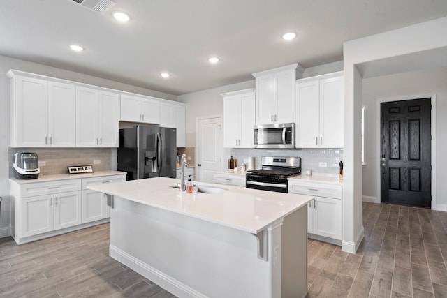 kitchen featuring appliances with stainless steel finishes, a sink, a center island with sink, and light wood-style floors