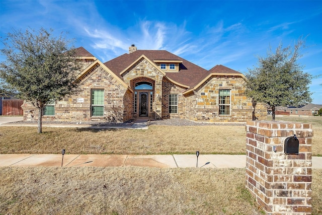 french country style house with stone siding, brick siding, a chimney, and a front yard