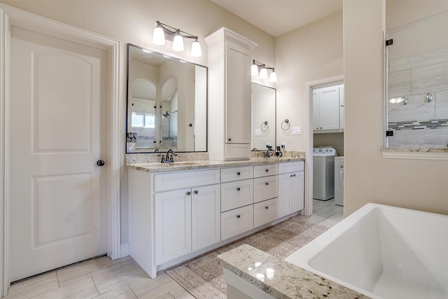 bathroom with double vanity, tiled shower, a washtub, separate washer and dryer, and a sink