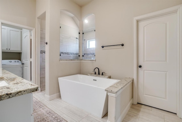 bathroom featuring washer / dryer, a tile shower, a freestanding bath, and vanity