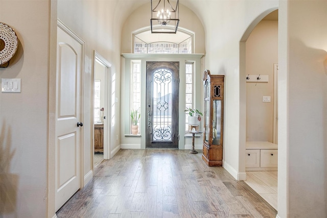 entrance foyer featuring arched walkways, light wood finished floors, a notable chandelier, and baseboards