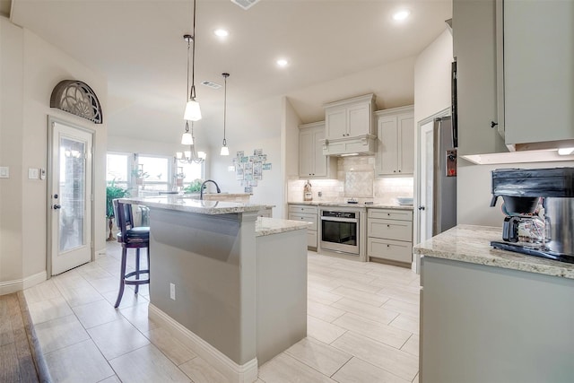 kitchen featuring tasteful backsplash, an island with sink, a breakfast bar area, hanging light fixtures, and stainless steel oven