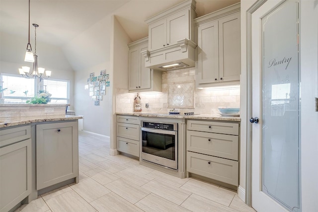 kitchen with pendant lighting, tasteful backsplash, lofted ceiling, light stone countertops, and oven