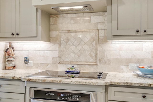 kitchen with black electric stovetop, oven, ventilation hood, light stone countertops, and tasteful backsplash