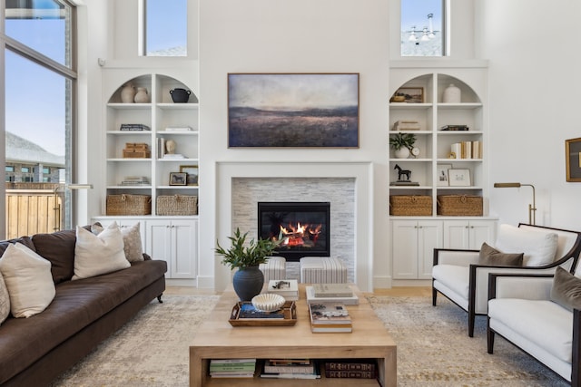 living room featuring built in shelves, a stone fireplace, and a high ceiling