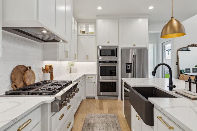 kitchen with white cabinets, custom range hood, appliances with stainless steel finishes, light wood-type flooring, and a sink