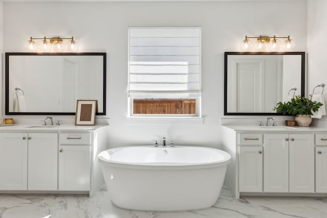 full bath featuring marble finish floor, two vanities, a sink, and a freestanding bath