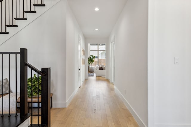 hallway featuring light wood-type flooring, recessed lighting, baseboards, and stairs