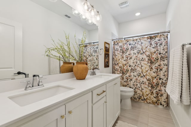 bathroom featuring toilet, double vanity, visible vents, and a sink